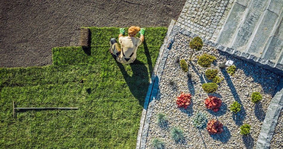 Decorative granite rock bed surrounds drought-tolerant shrubs beside stone pavers and a newly landscaped lawn area.