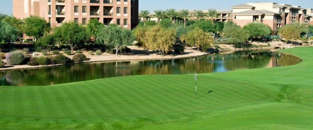 Overseeded green turf beside a clubhouse and landscaped pond on a Phoenix commercial property.